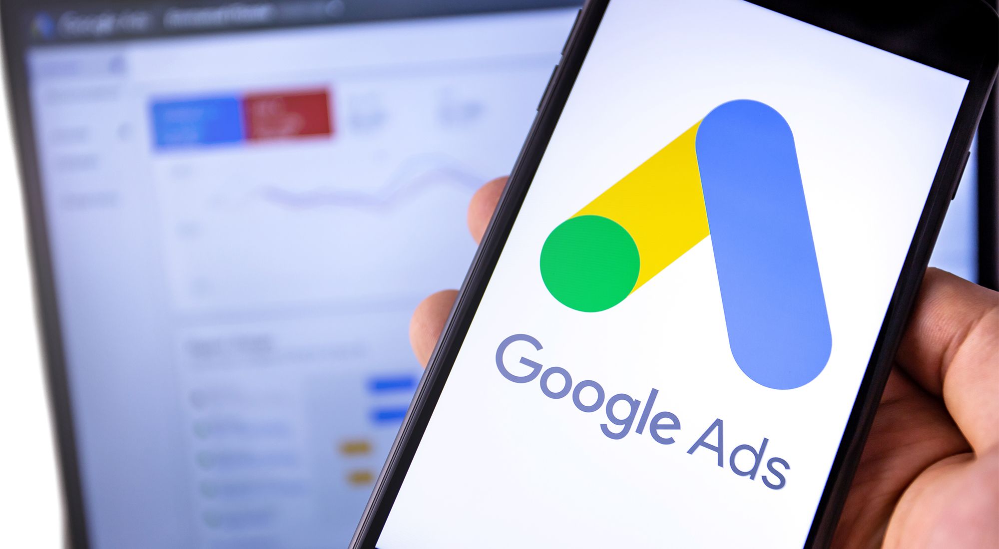 Google Ads logo on a phone with a laptop in background by Moonroute Media
